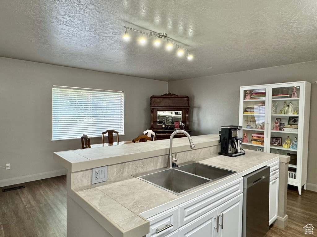 Kitchen with dishwasher, a sink, a textured ceiling, dark wood-type flooring, and white cabinetry