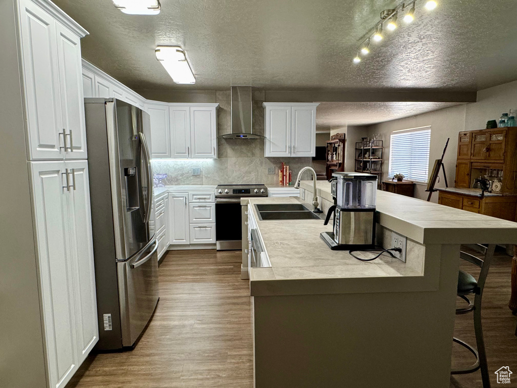 Kitchen with appliances with stainless steel finishes, wall chimney range hood, a sink, a textured ceiling, and dark wood finished floors