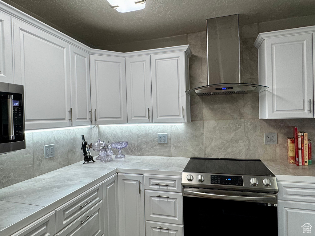 Kitchen with appliances with stainless steel finishes, wall chimney exhaust hood, light countertops, white cabinets, and a textured ceiling