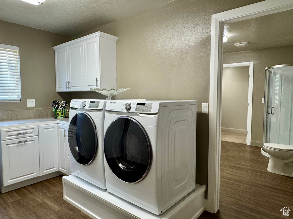 Washroom with dark wood-style flooring, independent washer and dryer, a textured wall, and a textured ceiling