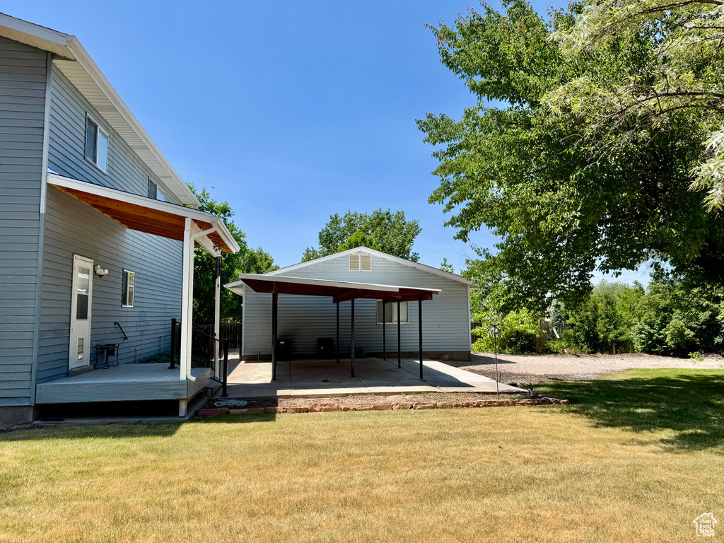 View of grassy yard with a wooden deck and a patio