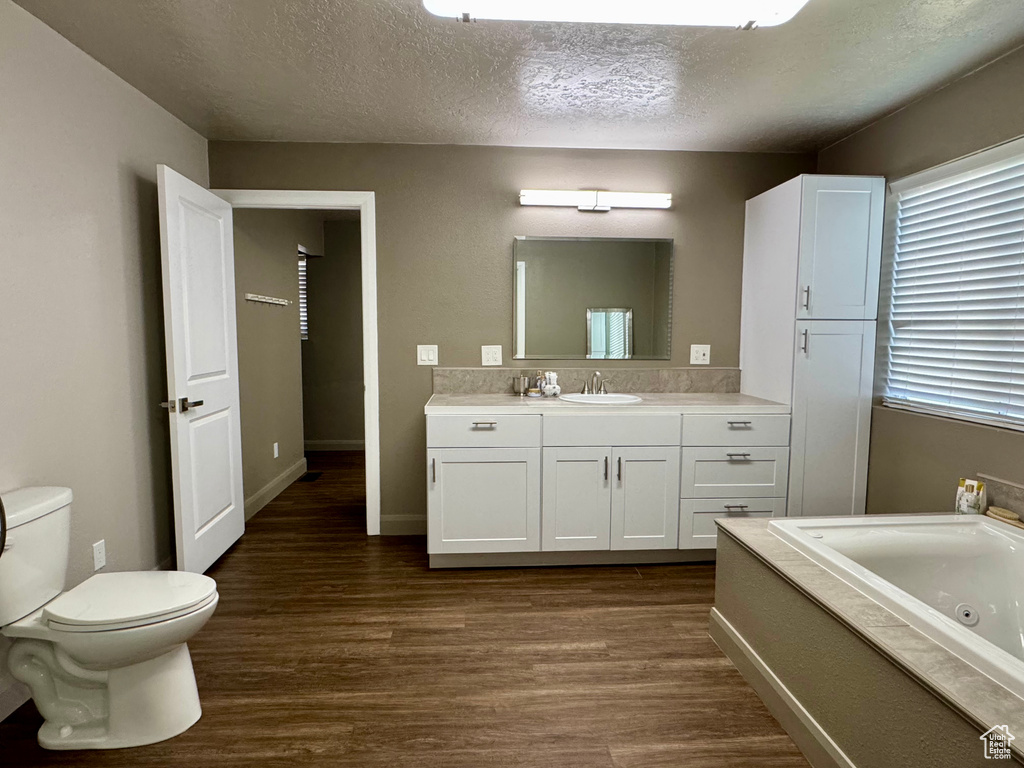 Full bathroom with wood finished floors, a jetted tub, vanity, toilet, and a textured ceiling
