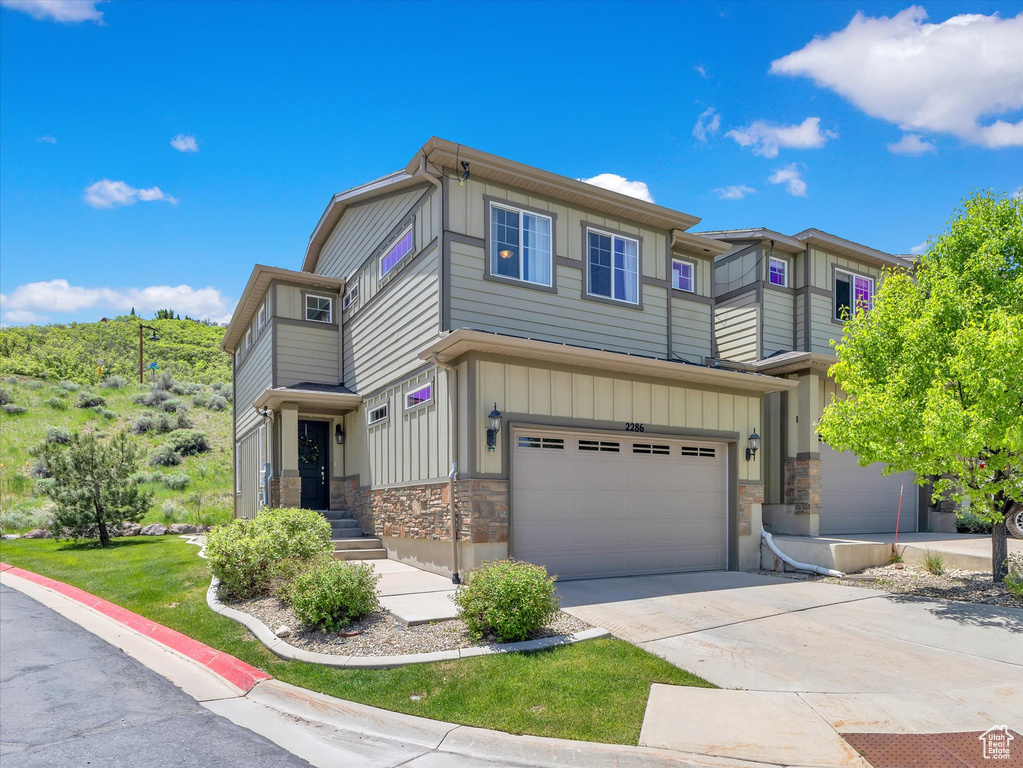 View of front facade featuring board and batten siding, an attached garage, stone siding, and concrete driveway