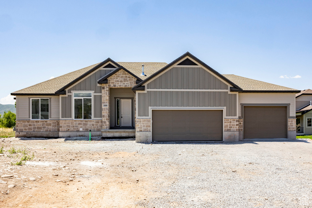 Craftsman-style home with stone siding, a garage, roof with shingles, and gravel driveway