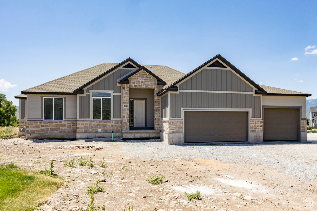 Craftsman-style home featuring stone siding, a garage, and roof with shingles