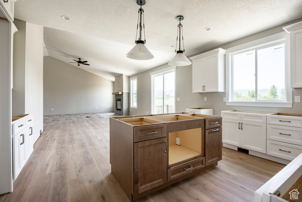 Kitchen with light wood finished floors, white cabinetry, decorative light fixtures, open floor plan, and a kitchen island