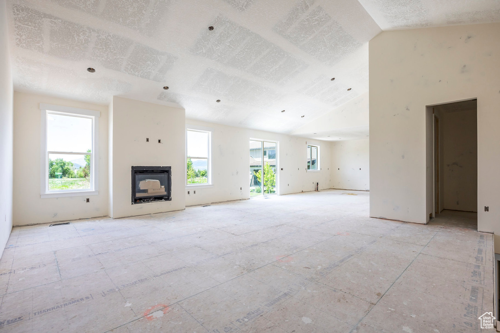 Unfurnished living room with lofted ceiling, a fireplace, and a textured ceiling