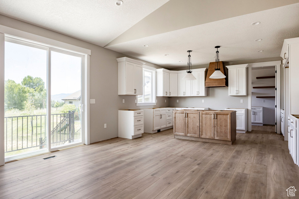 Kitchen with light wood finished floors, lofted ceiling, a center island, custom range hood, and hanging light fixtures