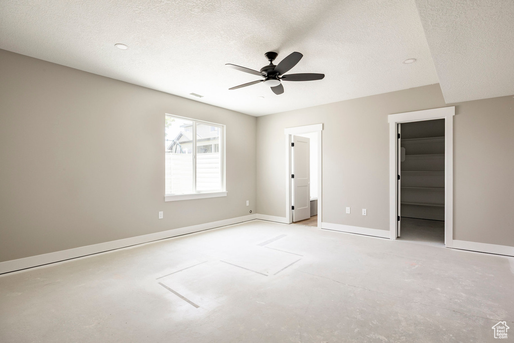 Unfurnished bedroom featuring a spacious closet, a textured ceiling, unfinished concrete floors, ceiling fan, and a closet