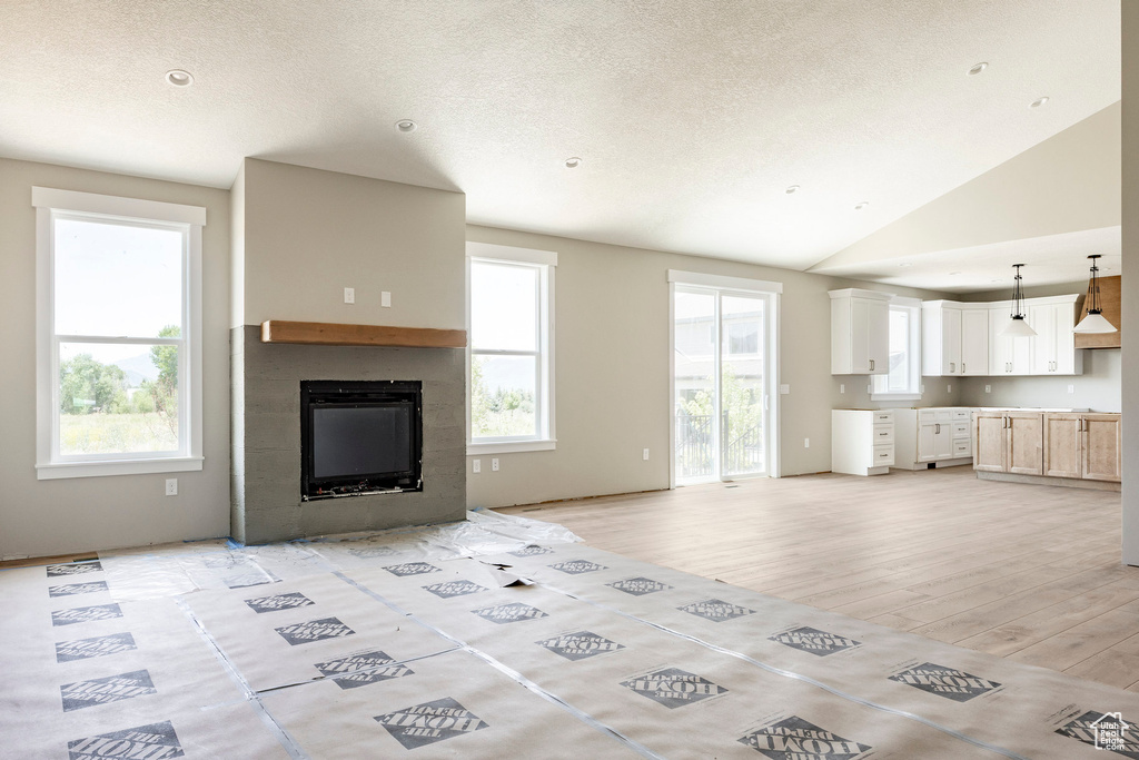 Unfurnished living room featuring a fireplace, plenty of natural light, light wood-style floors, lofted ceiling, and a textured ceiling
