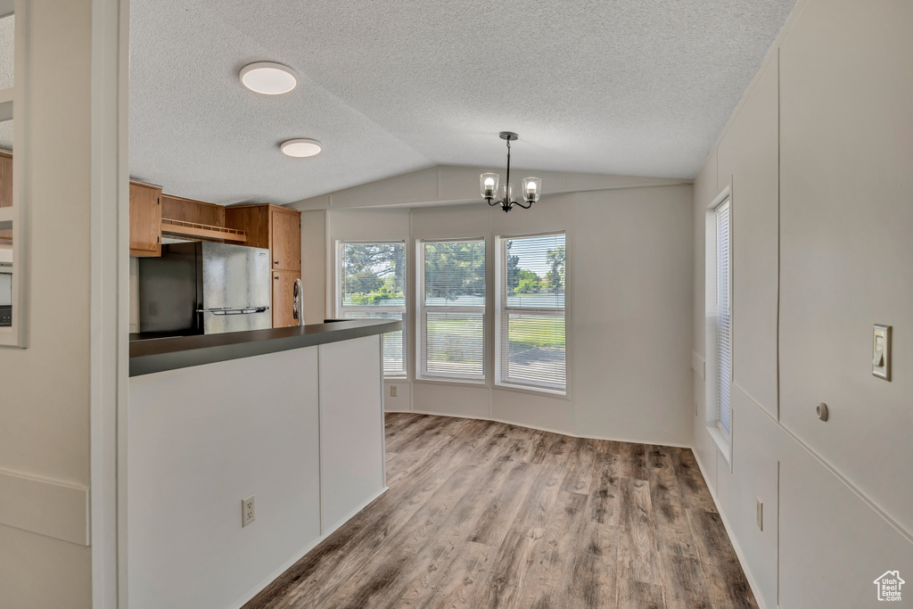 Kitchen featuring freestanding refrigerator, dark countertops, vaulted ceiling, brown cabinetry, and light wood-type flooring