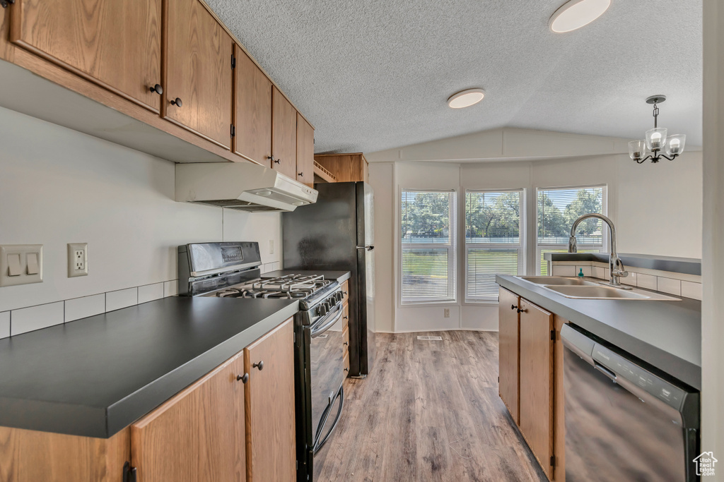Kitchen featuring stainless steel dishwasher, gas range, under cabinet range hood, a sink, and vaulted ceiling