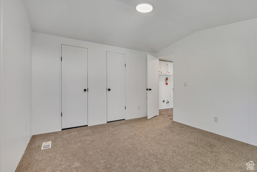Unfurnished bedroom with light carpet, vaulted ceiling, and multiple closets