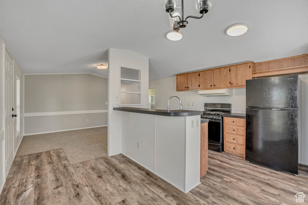 Kitchen with freestanding refrigerator, gas stove, exhaust hood, dark countertops, and light wood finished floors