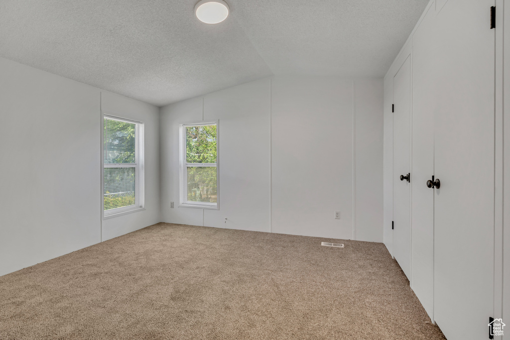 Carpeted spare room featuring lofted ceiling and a textured ceiling