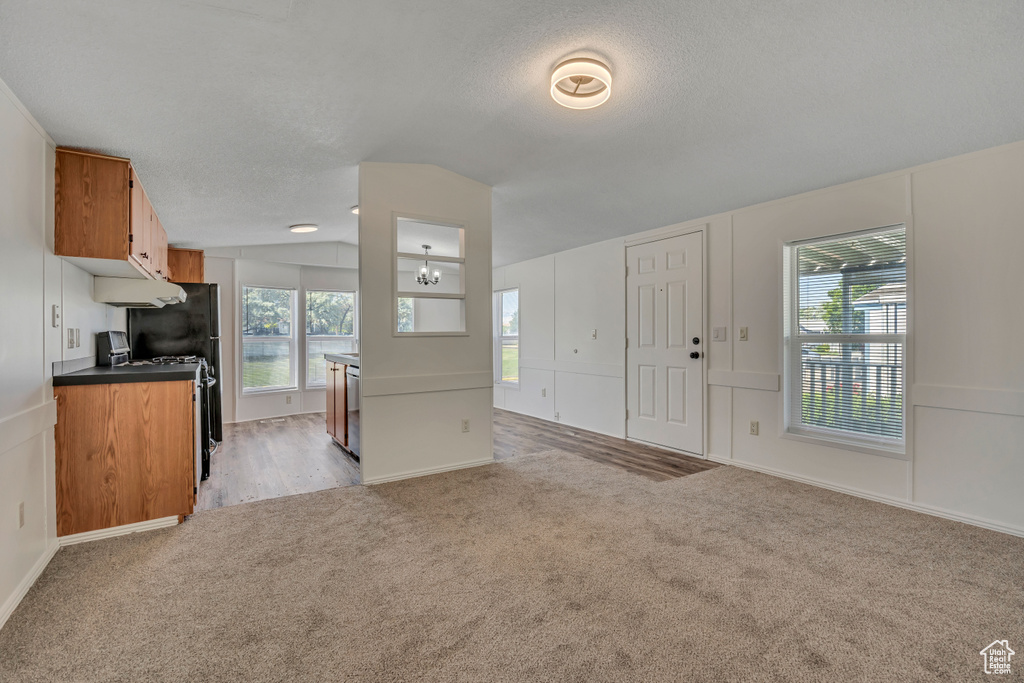 Kitchen with light colored carpet, vaulted ceiling, open floor plan, brown cabinets, and gas range