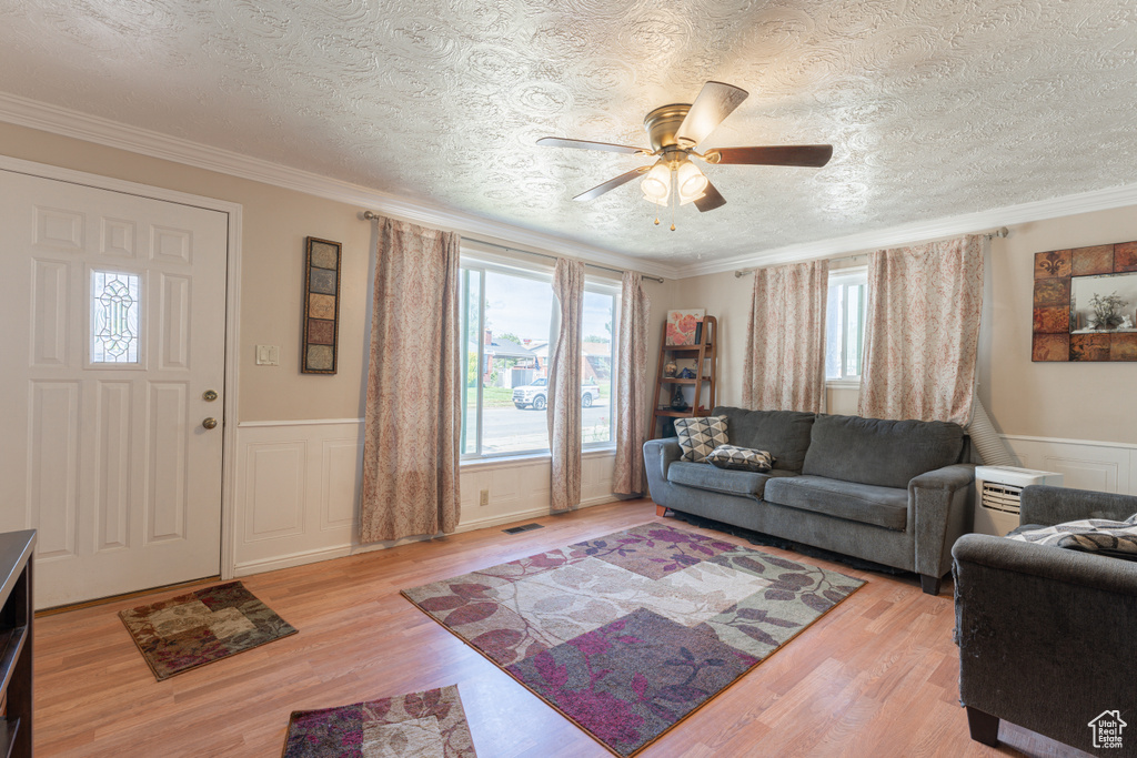 Living area with a wainscoted wall, a textured ceiling, ceiling fan, light wood finished floors, and ornamental molding