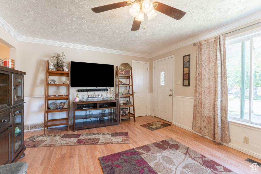 Entrance foyer with wood finished floors, a textured ceiling, a ceiling fan, crown molding, and a wainscoted wall