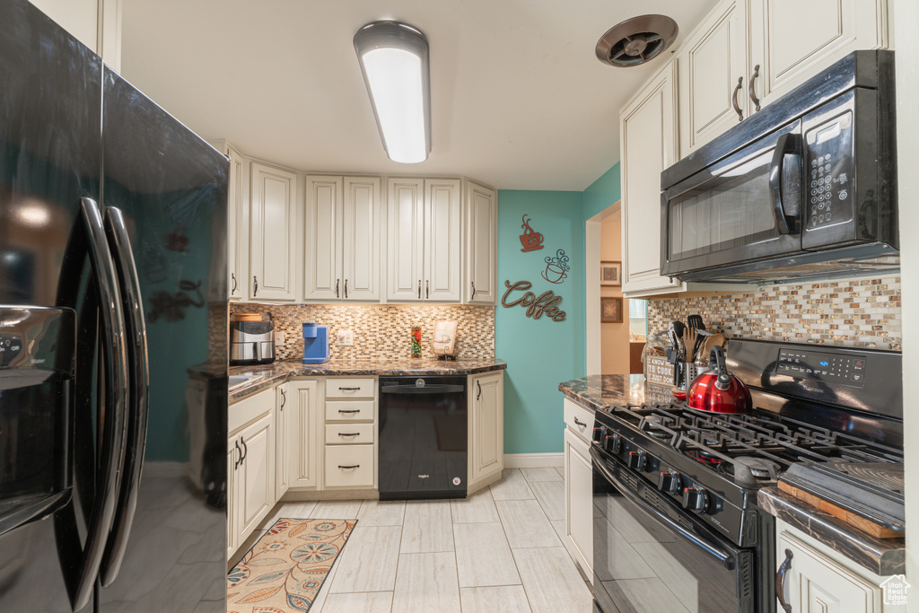 Kitchen with black appliances, backsplash, dark stone counters, baseboards, and cream cabinetry