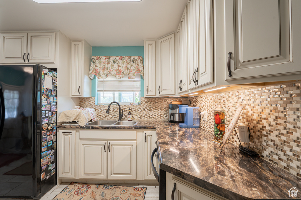 Kitchen with freestanding refrigerator, a sink, decorative backsplash, dark countertops, and light tile patterned floors