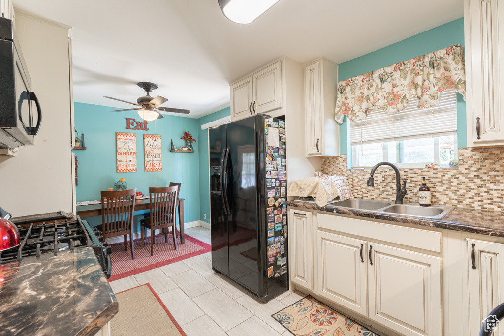 Kitchen featuring black refrigerator with ice dispenser, a sink, backsplash, stainless steel microwave, and dark countertops
