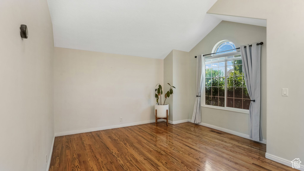 Empty room featuring wood finished floors, lofted ceiling, and baseboards