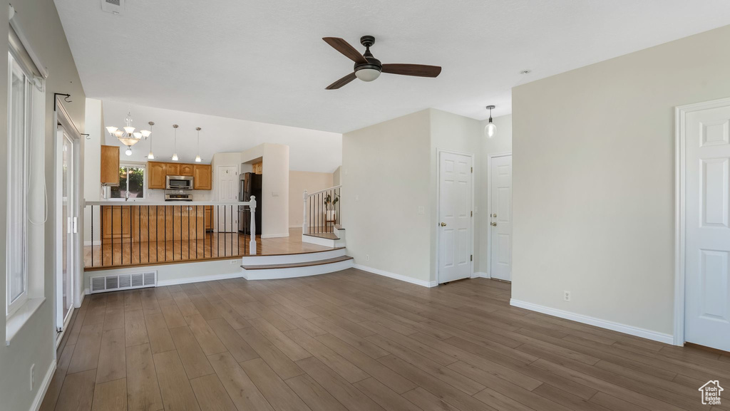 Unfurnished living room featuring a chandelier, ceiling fan, wood finished floors, and stairs