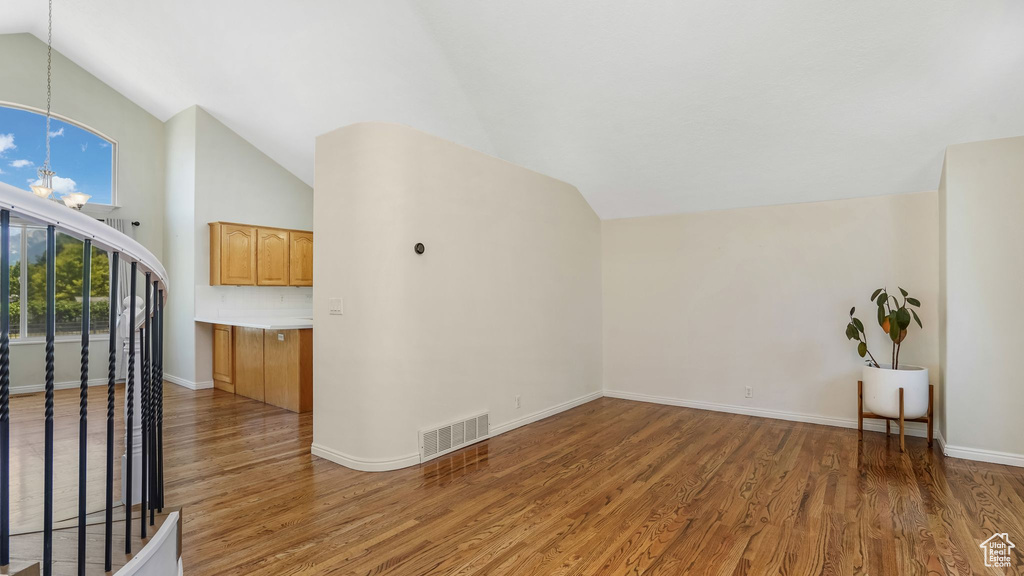 Unfurnished living room with vaulted ceiling, light wood-style flooring, a chandelier, and baseboards