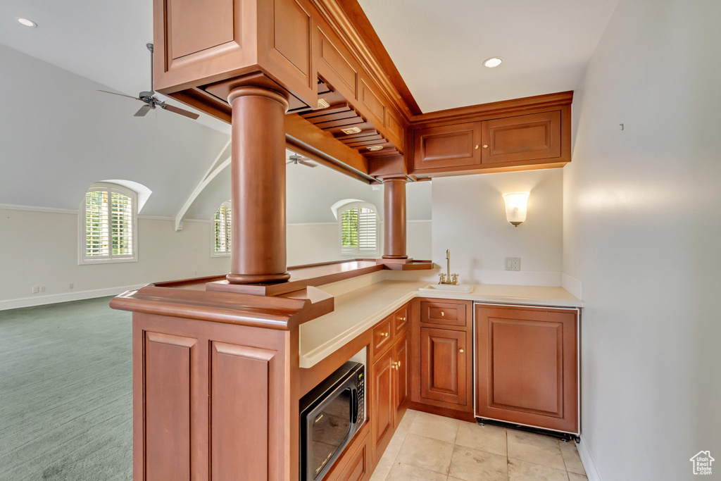 Kitchen featuring ceiling fan, kitchen peninsula, ornate columns, black microwave, and light colored carpet