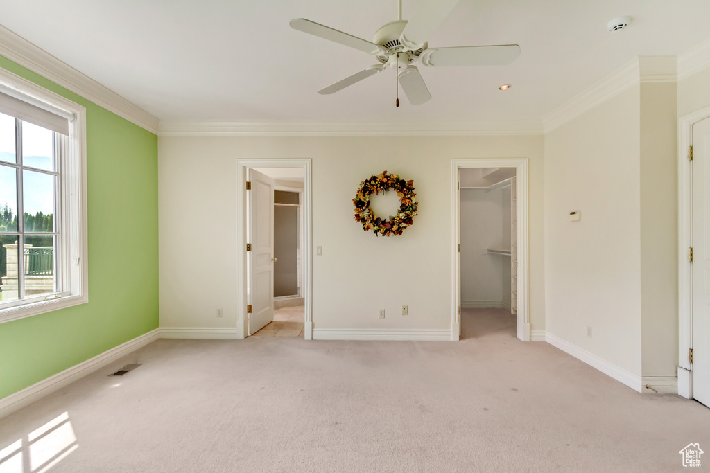 Unfurnished bedroom featuring a walk in closet, light colored carpet, and multiple windows