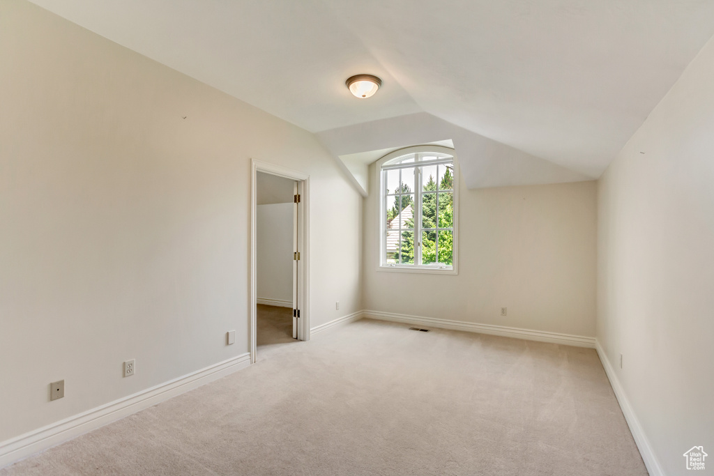 Unfurnished room featuring light carpet and vaulted ceiling