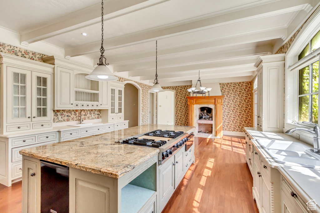 Kitchen with light stone counters, hanging light fixtures, a center island, beamed ceiling, and light wood-type flooring