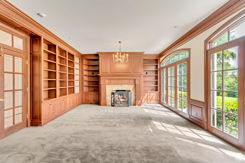 Unfurnished living room featuring built in shelves, plenty of natural light, light carpet, and crown molding
