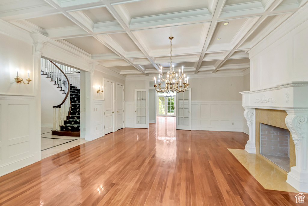 Unfurnished living room with a premium fireplace, beam ceiling, a chandelier, coffered ceiling, and hardwood / wood-style floors