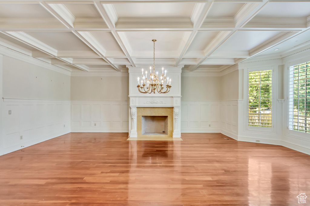 Unfurnished living room featuring beam ceiling, a notable chandelier, a fireplace, coffered ceiling, and light hardwood / wood-style floors