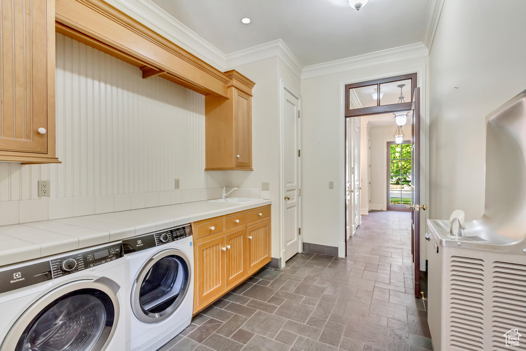 Clothes washing area featuring cabinets, sink, dark tile patterned flooring, ornamental molding, and independent washer and dryer