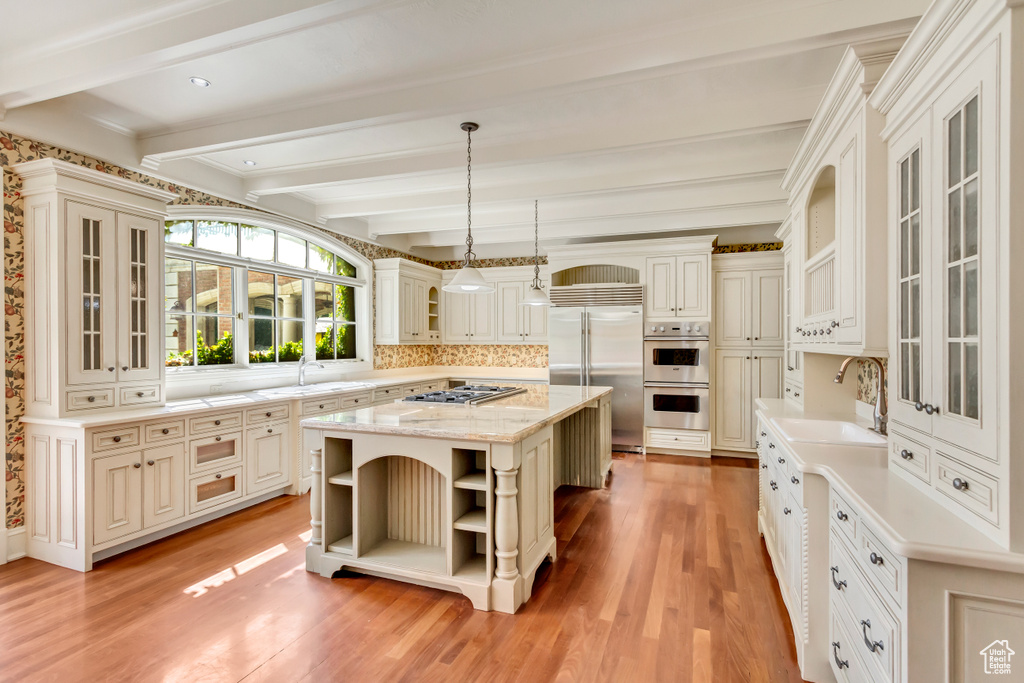 Kitchen with beam ceiling, a center island, light hardwood / wood-style floors, stainless steel appliances, and sink