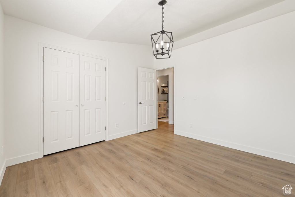 Unfurnished bedroom with a chandelier, light wood-style flooring, and baseboards