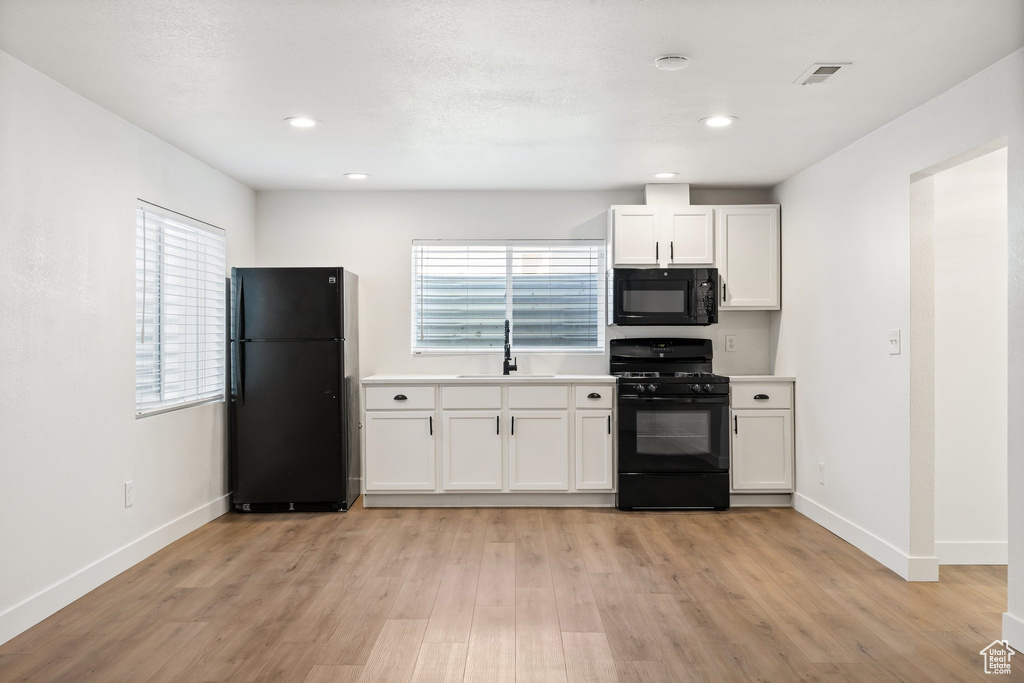 Kitchen with black appliances, a sink, light wood-style flooring, baseboards, and white cabinets