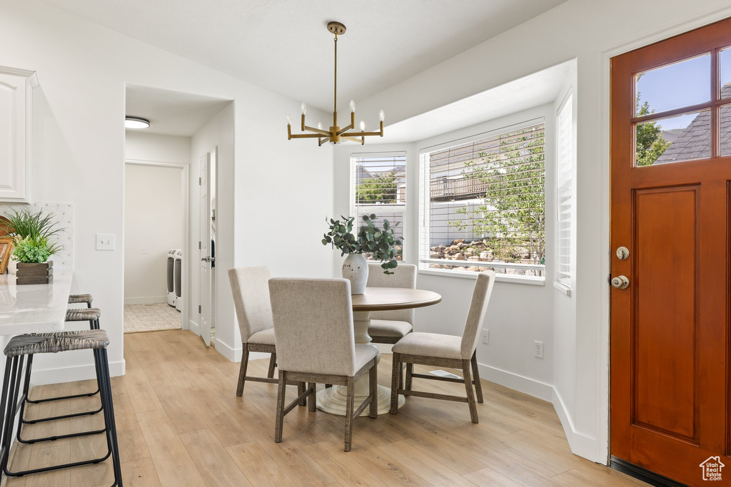 Dining area with a chandelier, light wood-style flooring, baseboards, and vaulted ceiling