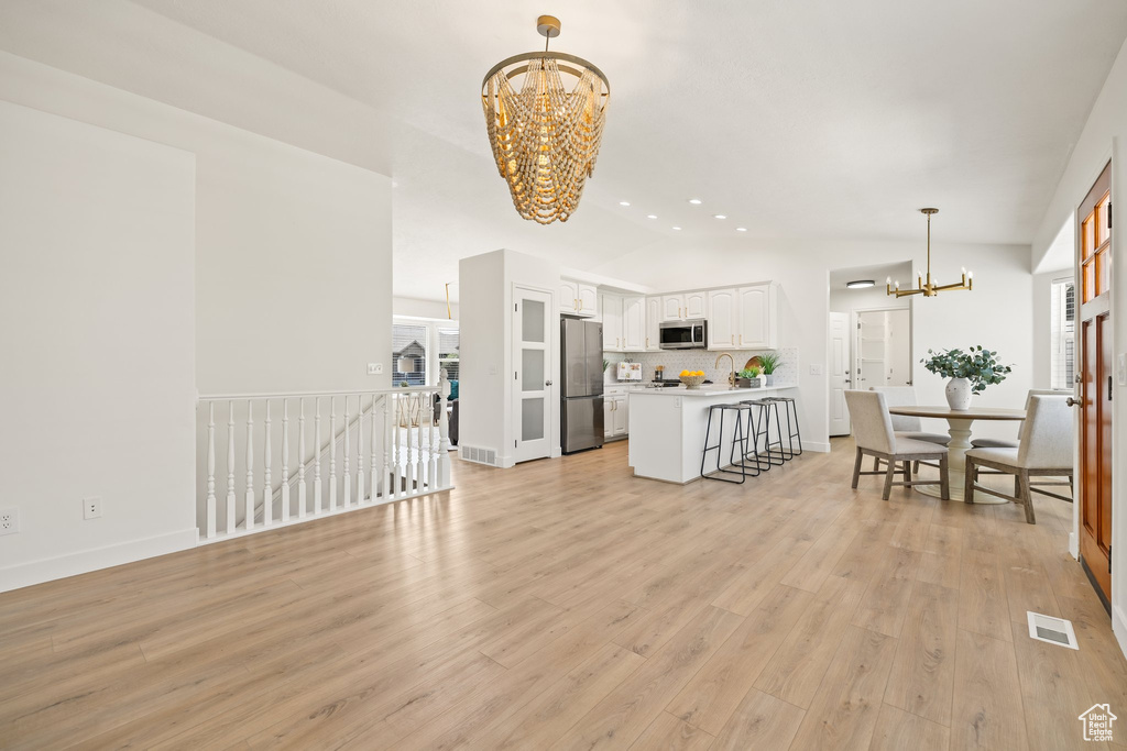 Living room featuring a chandelier, vaulted ceiling, light wood-style flooring, baseboards, and recessed lighting