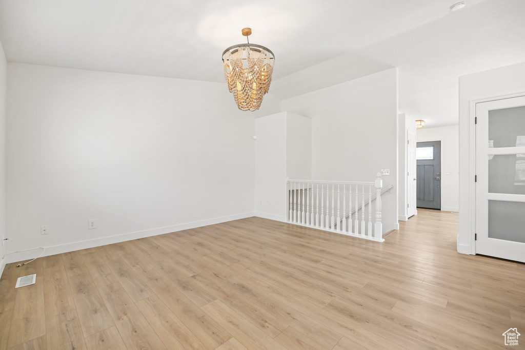 Empty room with a chandelier, light wood-style floors, and baseboards