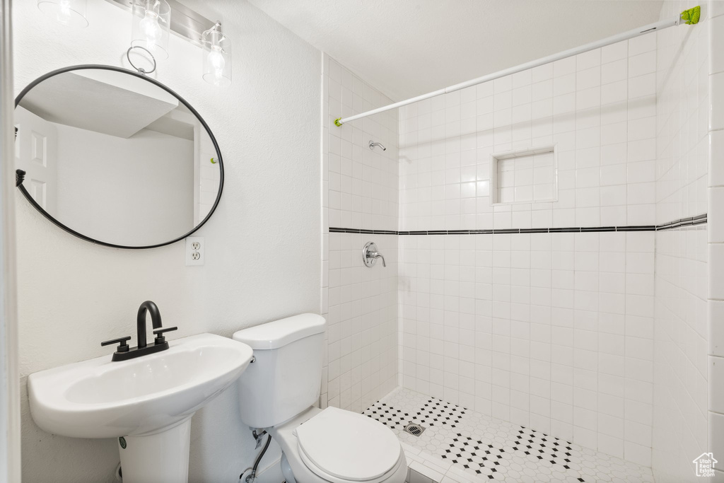 Bathroom with tiled shower, toilet, and a sink