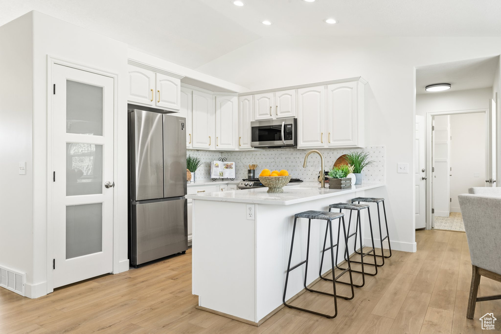 Kitchen featuring appliances with stainless steel finishes, a breakfast bar area, light wood-style floors, white cabinets, and lofted ceiling