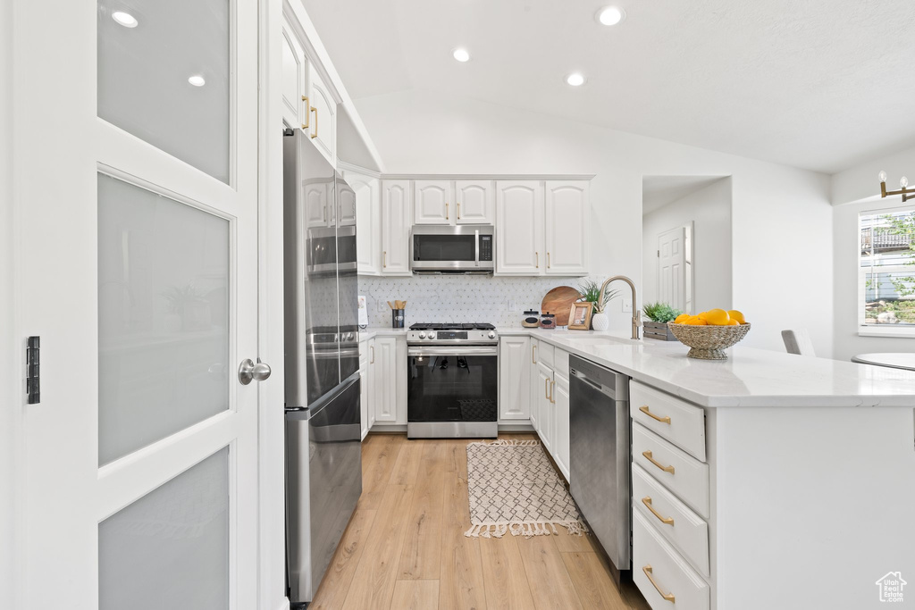 Kitchen with appliances with stainless steel finishes, a peninsula, a sink, lofted ceiling, and decorative backsplash