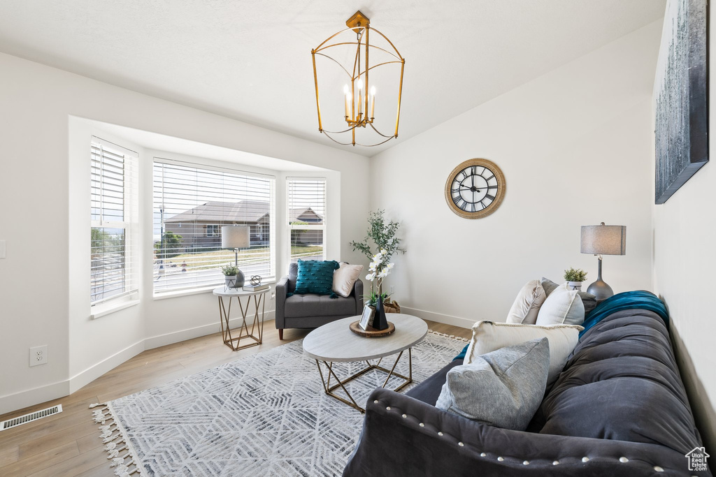 Living room featuring wood finished floors, a chandelier, baseboards, and lofted ceiling