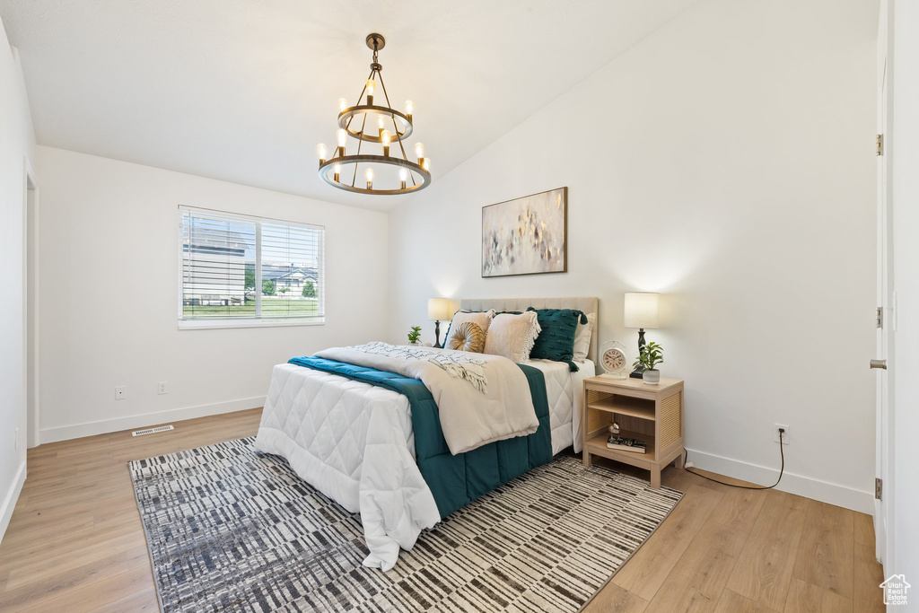 Bedroom with light wood-style flooring, baseboards, a chandelier, and lofted ceiling
