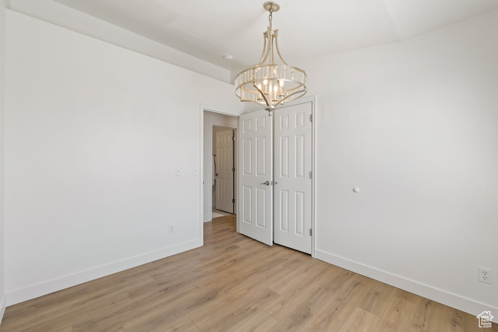 Spare room featuring baseboards, a chandelier, and light wood finished floors