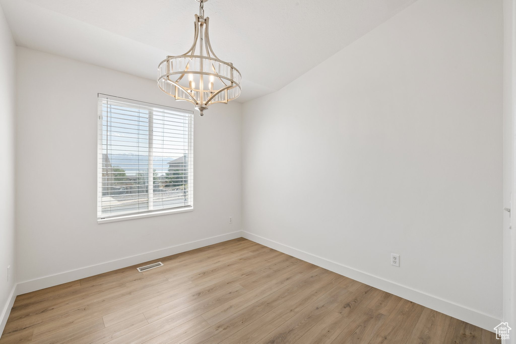 Spare room with a chandelier, baseboards, and light wood-style floors