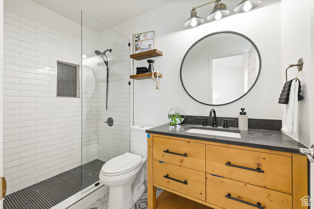 Bathroom with toilet, vanity, a tile shower, and marble finish flooring